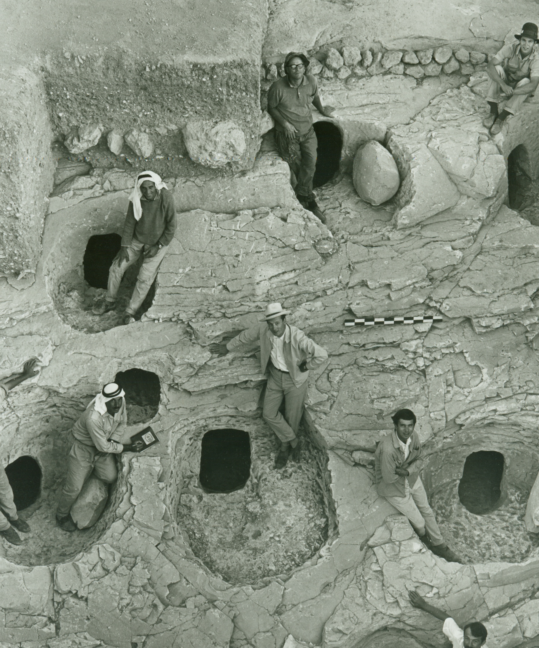 A group of archaeologists pose for a picture around a series of excavated tombs.