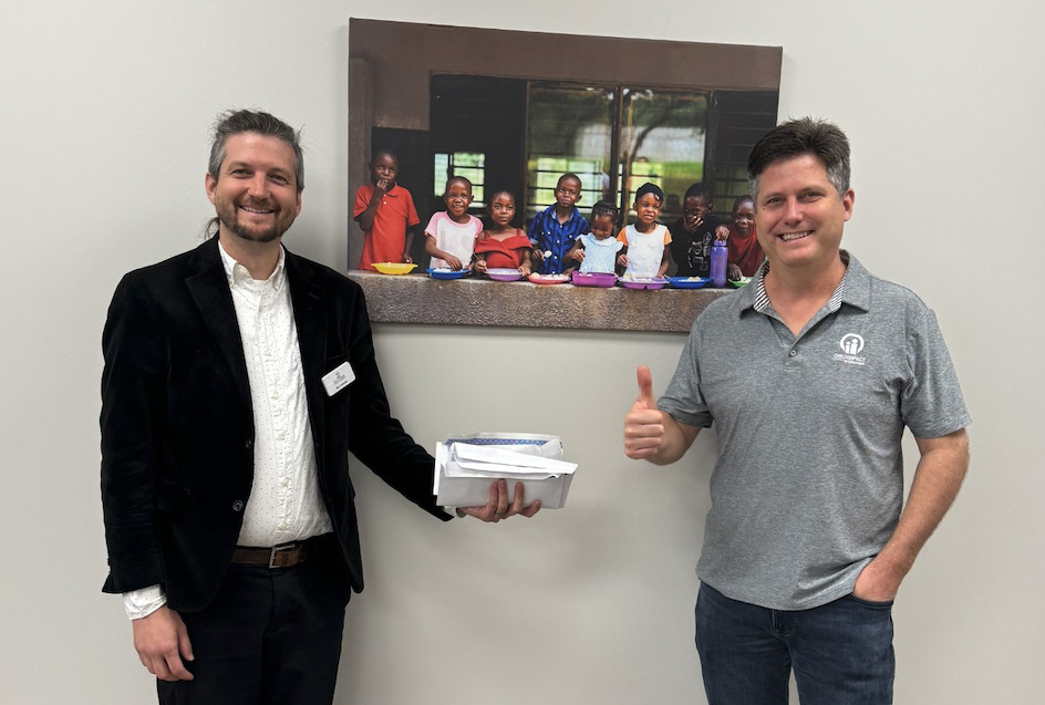 Southern Adventist University Professor Ben Schnell delivers funds raised by the Principles of Marketing class to Christopher Dubois Atib, director of development at Child Impact International.